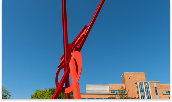 Red metal sculpture in front of a brick campus building under a clear blue sky
