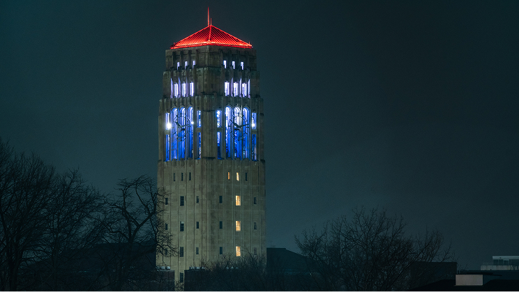 Lit Burton Memorial Tower at night, illuminated with blue and white lights and a red roof.