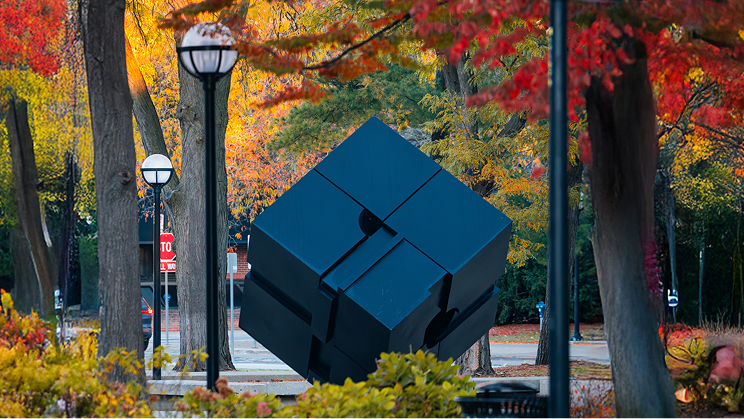 The Cube sculpture surrounded by autumn trees on the University of Michigan campus.