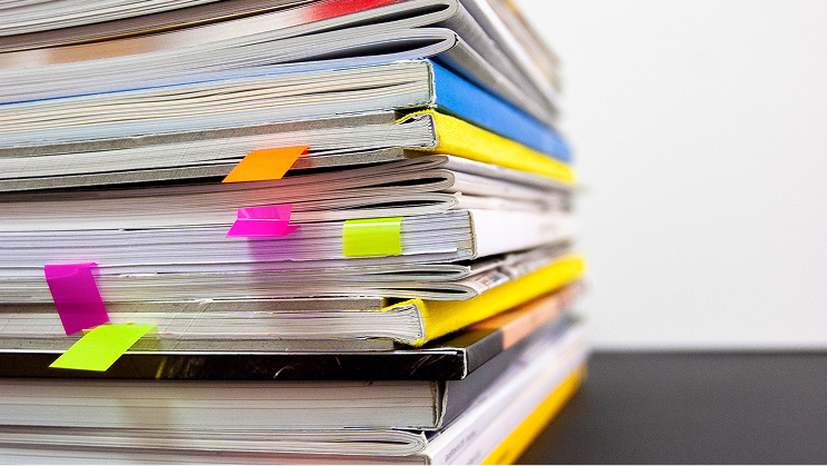 Stack of books and magazines with colorful sticky tabs marking pages.