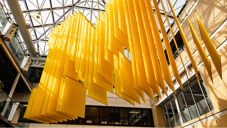 Hanging yellow panels art installation in a modern, glass-roofed atrium.