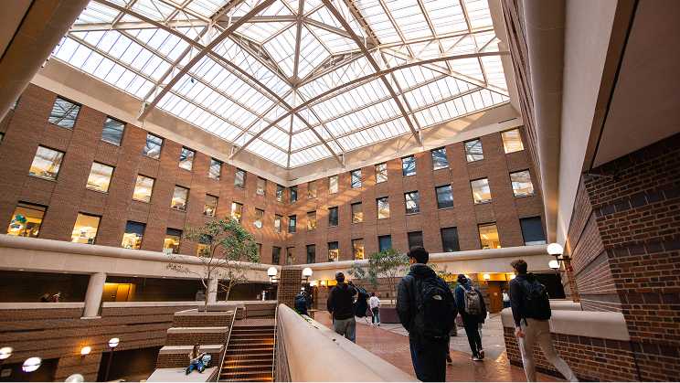 Students walking inside a large brick atrium with a glass ceiling.